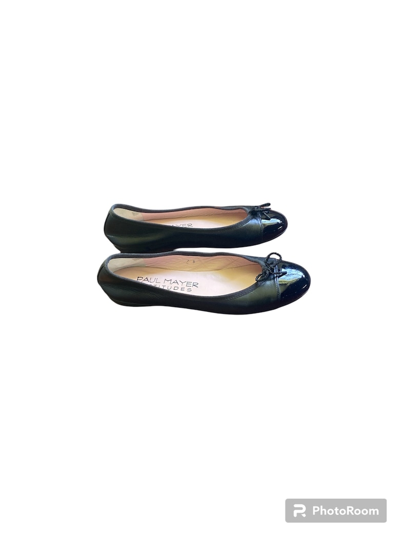 May include: A pair of black leather ballet flats with a black patent leather toe cap and a bow detail. The flats are by the brand "Paul Mayer Attitudes".