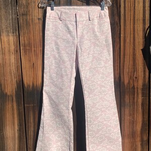 May include: A pair of wide-leg, bell-bottom pants in a light pink color with a white floral pattern.