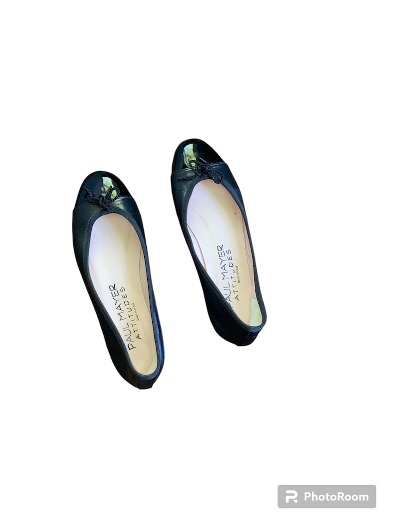 May include: A pair of black leather ballet flats with a patent leather toe. The flats have a bow on the toe and the words "Paul Mayer Attitudes" are printed on the insole.
