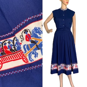 May include: A navy blue dress with a white and red embroidered band around the hem. The band features a repeating pattern of horses and a wagon.