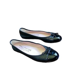 May include: A pair of black leather ballet flats with a patent leather toe cap and a black bow detail. The flats are made by Paul Mayer Attitudes.