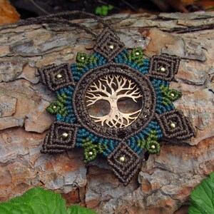 May include: A brown, green, and blue macrame necklace with a wooden tree of life pendant. The necklace is made with a starburst pattern and has small beads throughout.