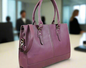Può includere: Una borsa tote in pelle viola con una tracolla lunga e due manici superiori. La borsa ha una chiusura a zip e una tasca frontale.