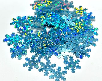 May include: A pile of iridescent blue snowflake sequins. The sequins are made of a shiny, holographic material that reflects light in a variety of colors.