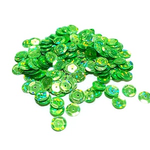 May include: A pile of green iridescent sequins, scattered on a white background. The sequins are round and have a slightly raised center.