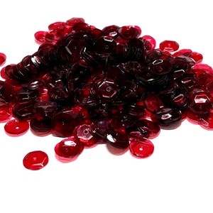 May include: A pile of red, iridescent sequins. The sequins are small and round, with a slightly raised center. They are perfect for adding sparkle to crafts and clothing.