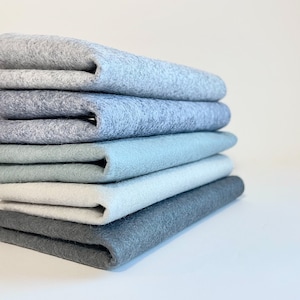 May include: Stack of six felt squares in shades of gray and blue, from dark gray to light blue.