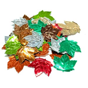 May include: Assortment of metallic leaf-shaped sequins in various colors, including green, silver, gold, copper, and red. The sequins are scattered on a white background.