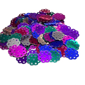 May include: A pile of colorful, metallic, flower-shaped sequins with small holes around the edges. The sequins are in shades of purple, pink, green, blue, and silver.