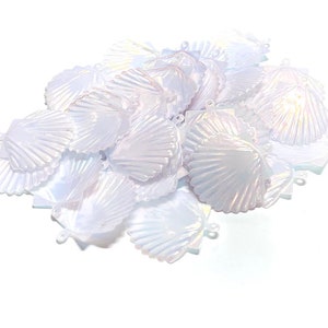 May include: A pile of white iridescent plastic seashells. The shells are all the same size and shape, and they are arranged in a random pattern.