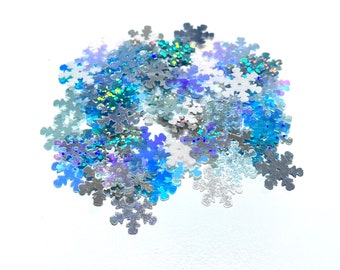 May include: A pile of iridescent blue and silver snowflake confetti. The snowflakes are scattered on a white background.