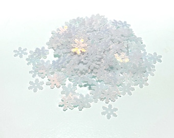 May include: A pile of iridescent white snowflake sequins. The sequins are scattered on a white background.