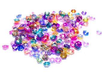 Op de afbeelding: Een grote stapel regenboogkleurige, bloemvormige pailletten in verschillende kleuren, waaronder roze, paars, blauw, groen en oranje.