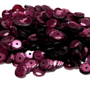May include: A large pile of burgundy sequins. The sequins are small and round with a slightly raised center.