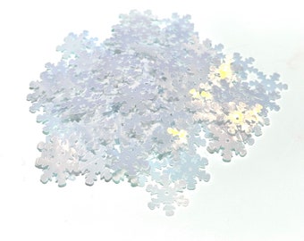 May include: A pile of iridescent snowflake-shaped sequins. The sequins are white with a subtle shimmer, catching the light. These decorative embellishments are ideal for crafts, scrapbooking, or holiday decorations.
