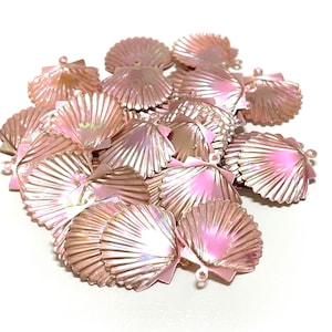 May include: A pile of iridescent pink plastic seashells with a hole at the top. The shells are arranged in a random pattern and are all the same size.