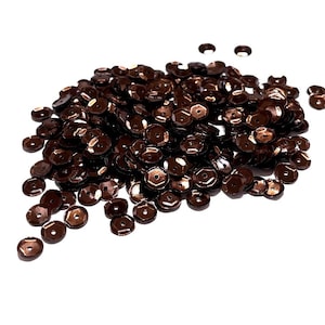 May include: A pile of brown metallic sequins. The sequins are small and round with a slightly raised center. They are perfect for adding a touch of sparkle to crafts and clothing.