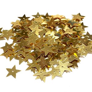 Può includere: Un grande mucchio di paillettes dorate a forma di stella. Le paillettes sono sparse su uno sfondo bianco.