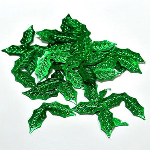 May include: A pile of green metallic holly leaves with a detailed design. The leaves are perfect for crafting and decorating.