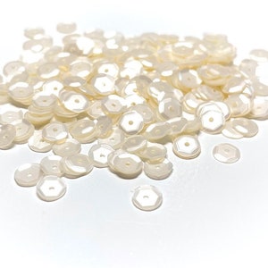 May include: A pile of white iridescent sequins, perfect for crafting and embellishing projects.