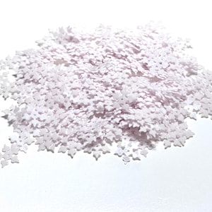 May include: A pile of small, white snowflake-shaped confetti. The confetti is scattered on a white surface, creating a wintery or festive appearance. Ideal for crafts, decorations, or holiday projects.
