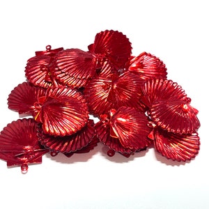 May include: A pile of shiny, red seashell charms. Each charm has a detailed, ridged texture and a small loop for attaching to jewelry or other crafts. The charms are clustered together against a white background.