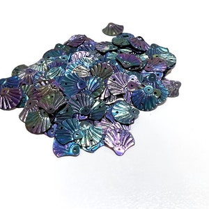 May include: A pile of iridescent blue, purple, and green seashell-shaped sequins. The sequins have a metallic finish and are perfect for adding a touch of sparkle to any craft project.