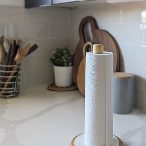 May include: White paper towel holder with a wooden base and a wooden top. The holder is on a white countertop in a kitchen.