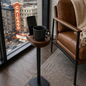 May include: A wooden side table with a black metal base and stem. The table holds a black mug and a smartphone. The background features a city view with a vintage "CHICAGO" sign and a leather armchair.