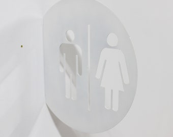 May include: A white, semi-circular restroom sign with cut-out male and female figures. The sign is mounted on a white wall, with the figures separated by a vertical line. The sign is designed for public restrooms.