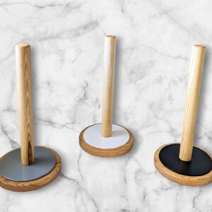 May include: Three wooden paper towel holders with different colored bases. The bases are white, gray, and black.