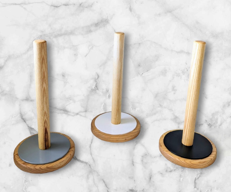 May include: Three wooden paper towel holders with different colored bases. The bases are white, gray, and black.
