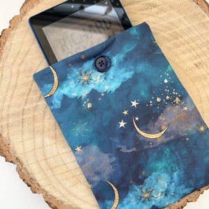May include: An e-reader case made of blue and gold fabric with a crescent moon and star pattern. The case has a button closure.