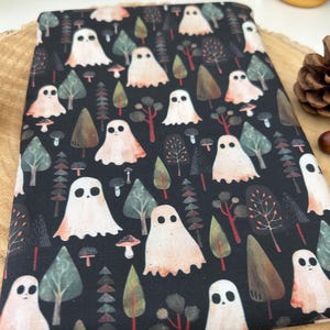 Black fabric book cosy featuring a repeating pattern of white ghosts, trees, and mushrooms. The ghosts have a simple, rounded shape with two black eyes. The trees are various shades of green and brown. The design has a spooky, Halloween theme.