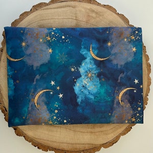 A dark blue book sleeve with a celestial design featuring gold  coloured crescent moons, stars, and clouds. The sleeve holds a book. The book sleeve is made of fabric.
