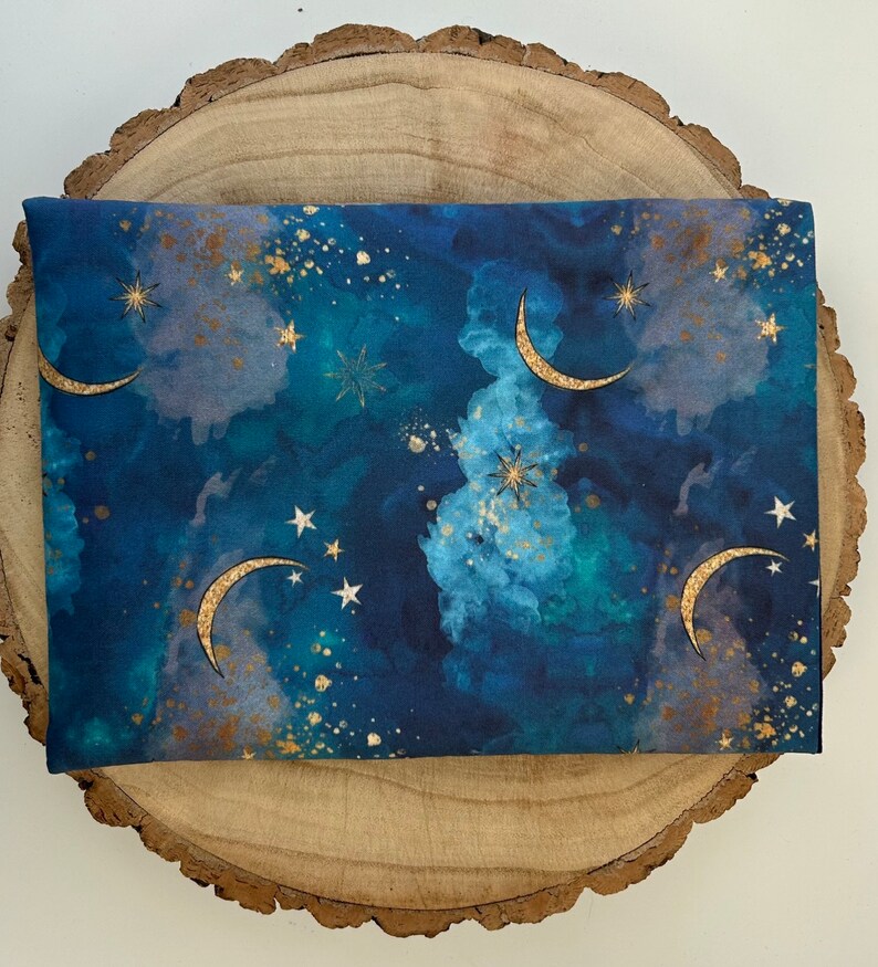 A dark blue book sleeve with a celestial design featuring gold  coloured crescent moons, stars, and clouds. The sleeve holds a book. The book sleeve is made of fabric.