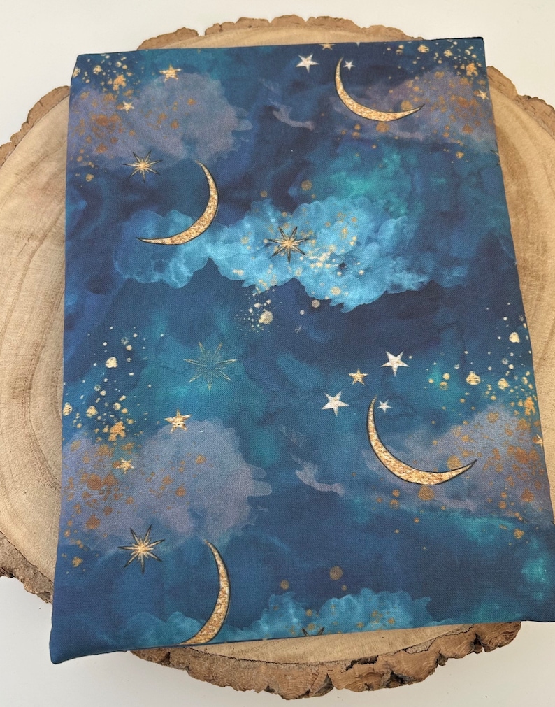 A dark blue book sleeve with a celestial design featuring gold  coloured crescent moons, stars, and clouds. The sleeve holds a book. The book sleeve is made of fabric.
