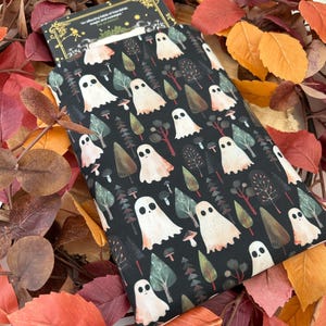A black book sleeve with a repeating pattern of white ghosts, trees, and mushrooms. A book is partially visible. Autumn leaves form the background.
