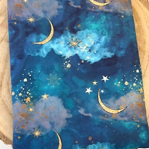 A dark blue book sleeve with a celestial design featuring gold  coloured crescent moons, stars, and clouds. The sleeve holds a book. The book sleeve is made of fabric.