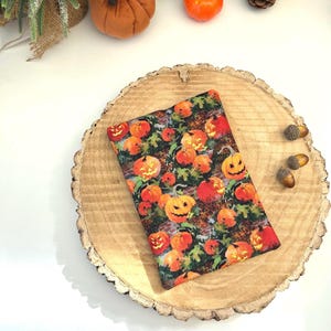 May include: A rectangular fabric pouch featuring a repeating pattern of orange jack-o'-lanterns with carved faces, green leaves, and dark foliage on a textured background. The pouch has a flat, soft construction with a visible seam along the edge.