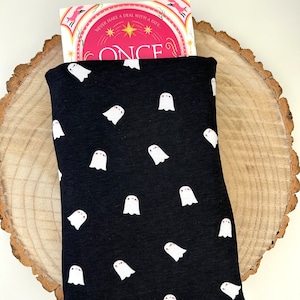 May include: A black book sleeve with a white ghost pattern. The sleeve is holding a pink and white book with the title "Once" and the text "Never make a deal with a fate".