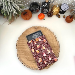 May include: A burgundy and brown owl-patterned tablet sleeve with a button fastening. The sleeve displays a repeating design of owls, leaves, and berries. The tablet is partially visible inside the sleeve, which is on a wooden slice.