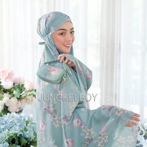 May include: A light blue prayer shawl with a floral print and a small matching bag. The shawl has a lace trim and the bag has a gold clasp. The text "JUNGKELBOY" is visible on the shawl.