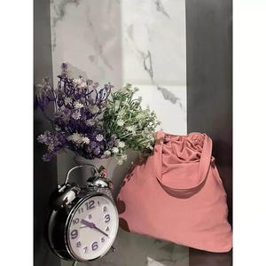 May include: A pink fabric tote bag with a drawstring closure and a silver alarm clock with a white face and black hands. The clock is set to 12:00. The bag and clock are on a white and gray marble surface.
