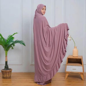 May include: A mauve prayer dress with a ruffled hem. The dress is made of a soft, flowing fabric and has a simple, elegant design.