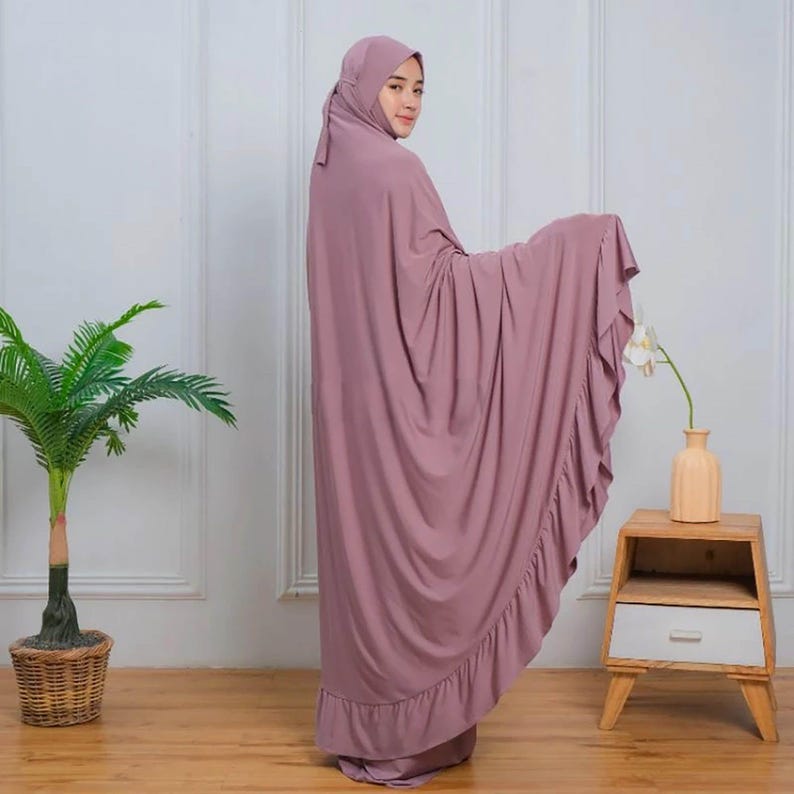 May include: A mauve prayer dress with a ruffled hem. The dress is made of a soft, flowing fabric and has a simple, elegant design.