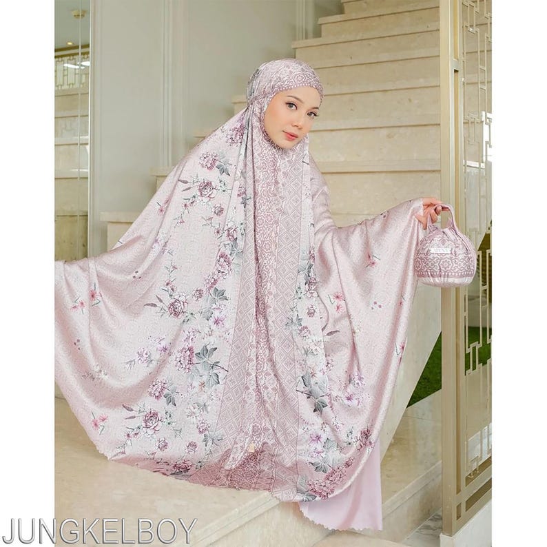 Pu&ograve; includere: Un completo da preghiera rosa chiaro con un motivo floreale, che include un copricapo, una veste e una piccola borsa abbinata. Il set presenta un design delicato con sfumature di rosa, viola e verde. L'indumento &egrave; indossato su una scala.