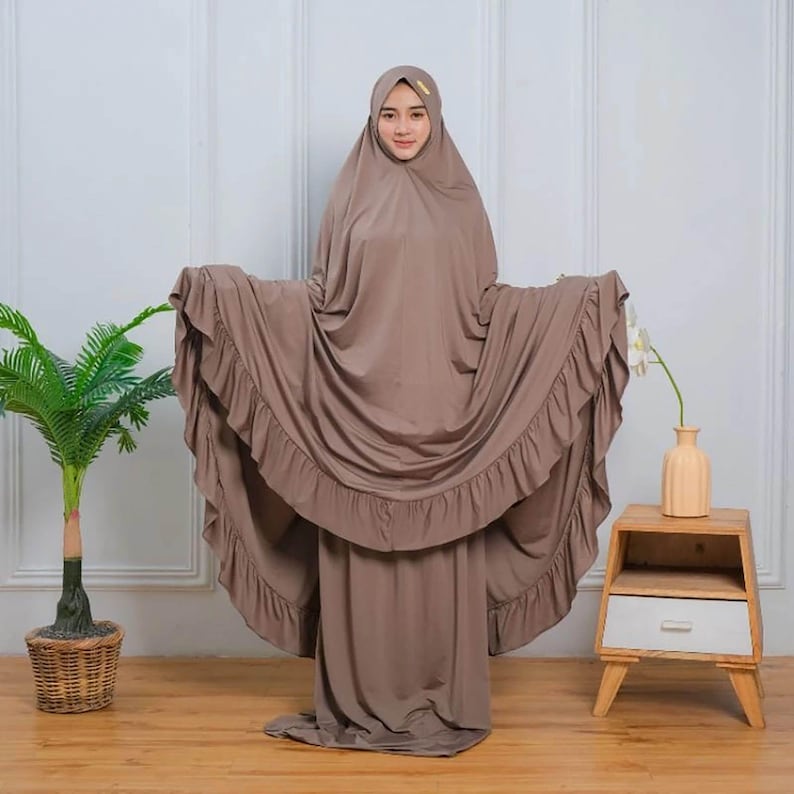 May include: A brown prayer dress with a ruffled hem and matching headscarf. The dress is made of a soft, flowing fabric.