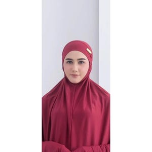 May include: A burgundy prayer dress with long sleeves and a matching head covering. The head covering has a gold accent.