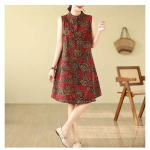 May include: Sleeveless red dress with a floral pattern. The dress has a high neckline and a knee-length hemline. The floral design includes brown and tan roses. The dress is worn by a person.